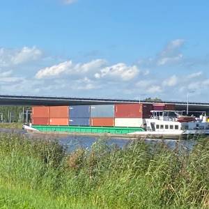 Containerschip vaart met autokraan tegen brug over kanaal